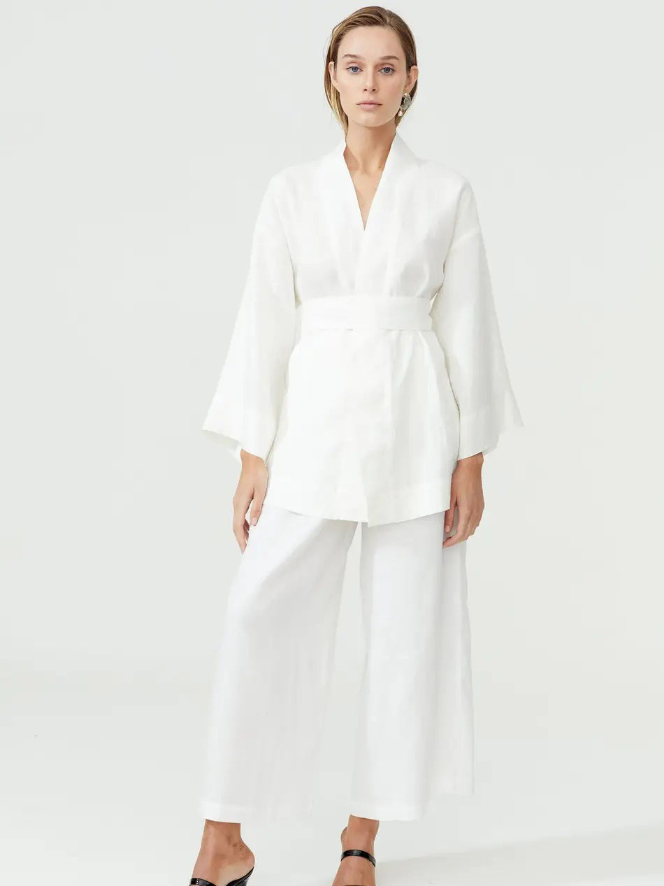 A person with light-colored hair is wearing a black LANHTROPY KENIA Kimono Linen Jacket with a self-tie belt and light gray jeans. They have their right hand in their pocket and are standing against a plain white background.