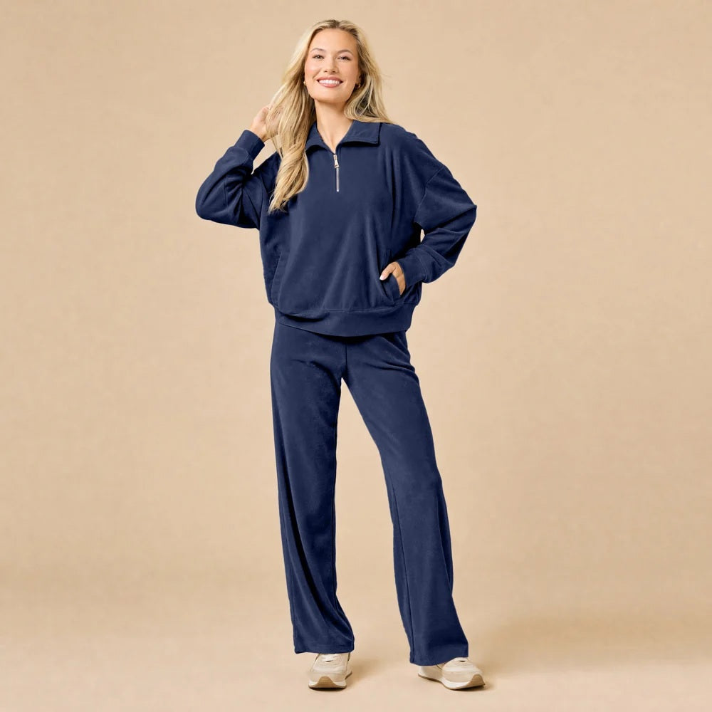 A woman seated on the floor wearing a Softies - Serenity 1/4 Zip Top with Wide Leg Pant lounge set in midnight, featuring a navy blue quarter-zip pullover and matching wide-leg lounge pants.