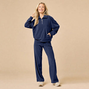 A woman seated on the floor wearing a Softies - Serenity 1/4 Zip Top with Wide Leg Pant lounge set in midnight, featuring a navy blue quarter-zip pullover and matching wide-leg lounge pants.