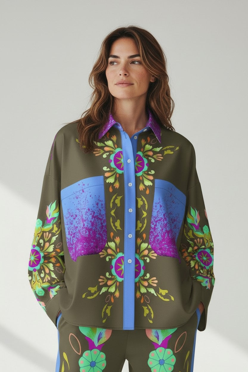 A woman with wavy brown hair wears the FRANCO FERRARI Silk Blouse, featuring colorful blue, purple, and green floral patterns and large front pockets, standing against a light background and smiling slightly to the side.