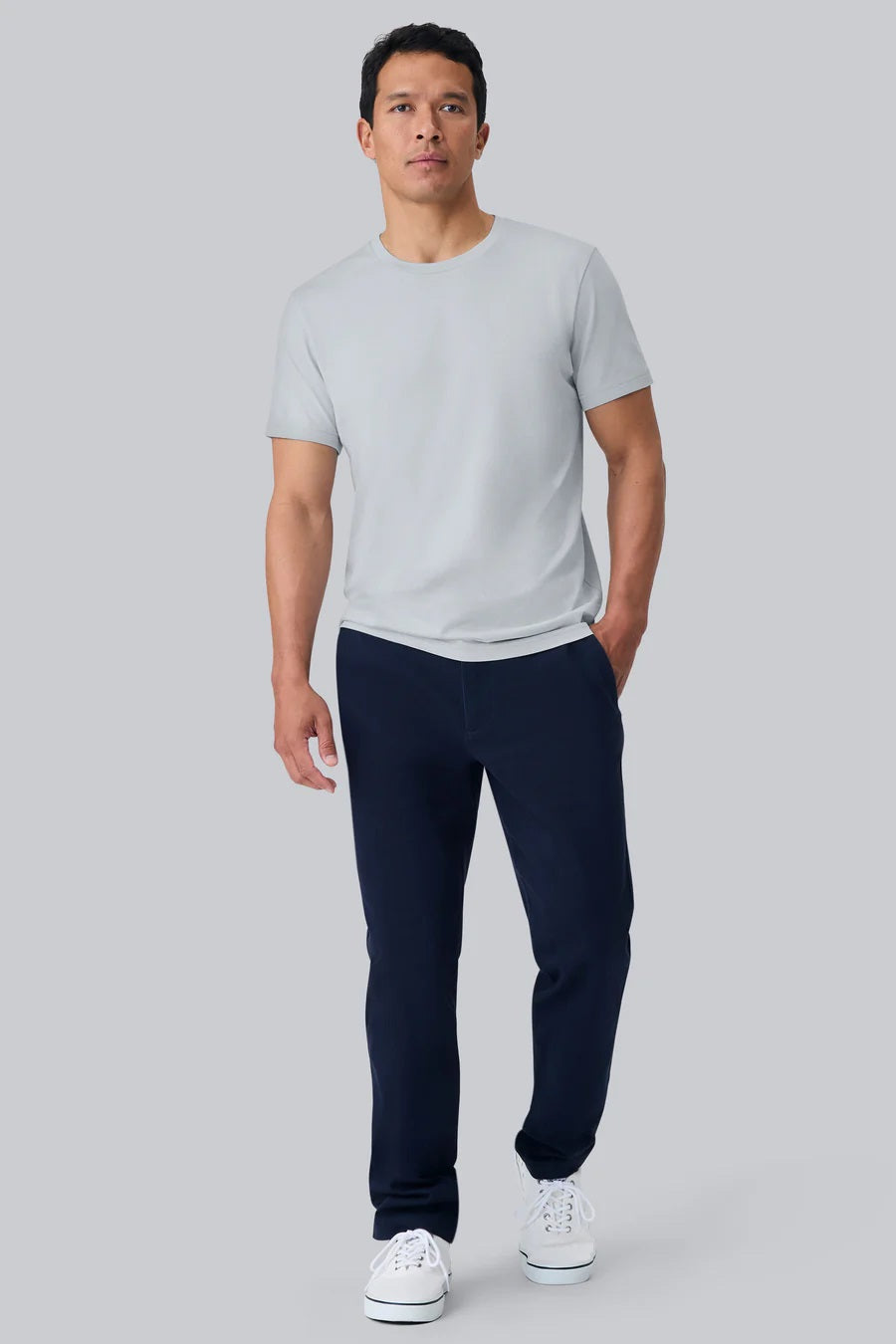 A man with short dark hair wears the MACK WELDON Pima Crew Neck T-Shirt in Steam and dark pants, standing against a plain light gray background and looking at the camera with a neutral expression.