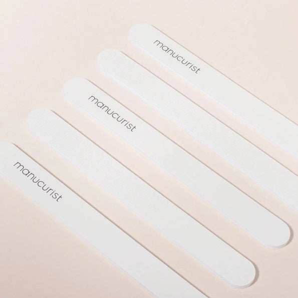 Five MANUCURIST - EMERY BOARD nail files from MANUCURIST INC, each featuring the brand’s logo, are arranged diagonally on a light beige background.