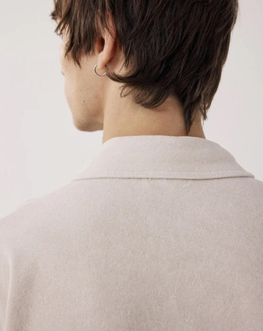 Wearing the HARTFORD Terry Polo Shirt in Stone with sage green cargo pants, a person stands with one hand in their pocket, glancing to the side against a plain background.