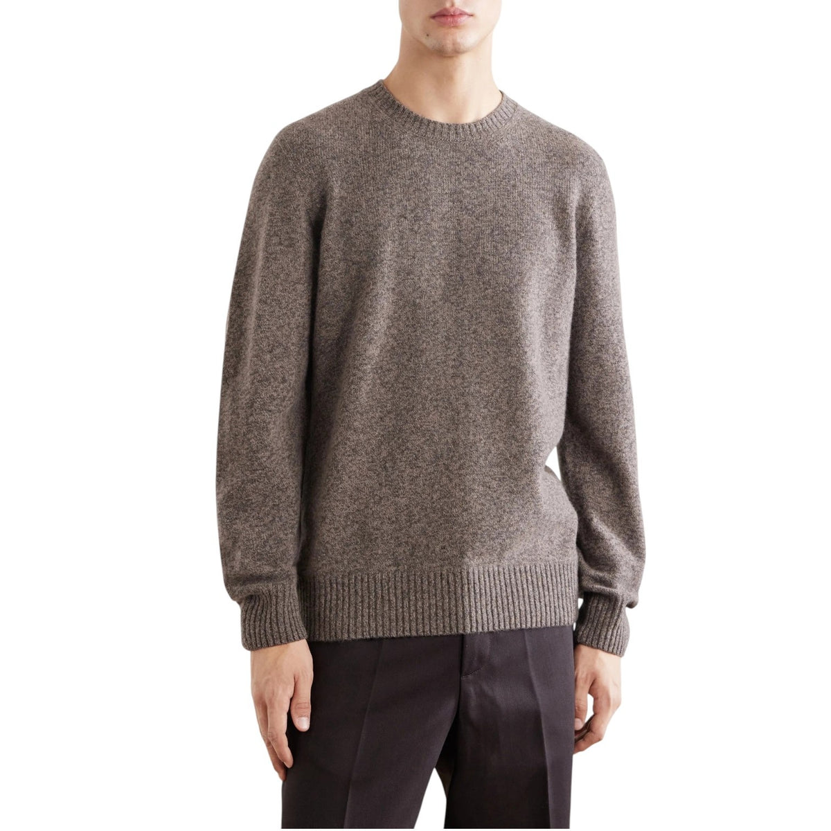 A person wearing the HARTFORD Seamless Wool Crew Pullover in Mushroom, an Italian-made sweater, paired with dark pants, is seated with one arm resting on their knee against a plain light background.