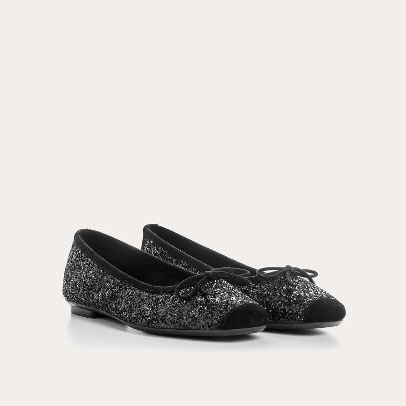 The REQINS Harmony Sequin Ballerina Flats in Noir feature black sequins, black toe caps, and small bows—bringing a touch of everyday luxury against a plain light background.