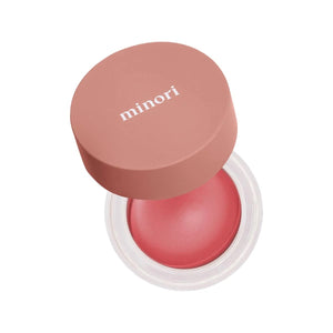 An open jar of MINORI - CREAM BLUSH in the shade Sweet Pea, featuring a pink lid and revealing a smooth, rosy pink cream-to-powder formula inside the clear container for a natural-looking blush finish.