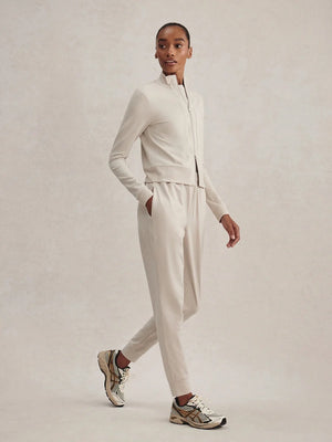 A person wears a light beige Varley Rufus Cropped Zip Through Sweat in Pebble Marl with a high collar and matching pants.