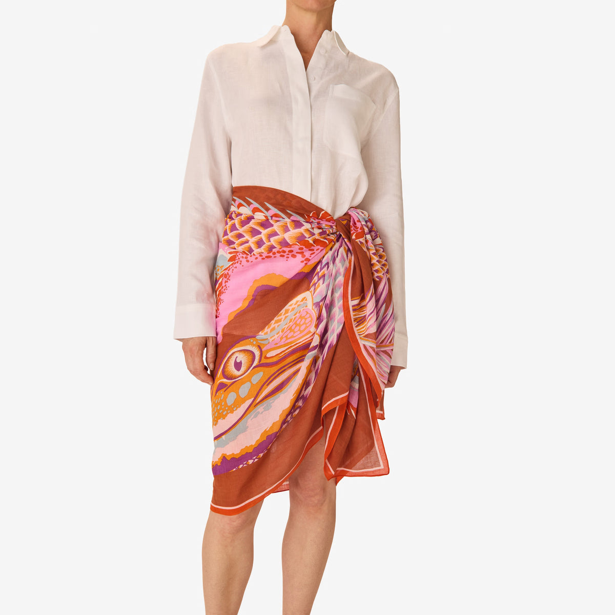 A woman in a sleeveless beige dress stands against a white background, wearing the INOUI EDITIONS - CROCO SCARF IN CARAMEL by INOUI, draped over her left shoulder and around her neck.