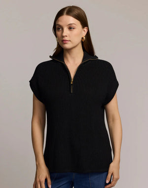 A woman with straight brown hair wears the HINSON WU - BROOKE SLEEVELESS SWEATER VEST in black with a gold-tone half-zip and blue jeans, standing facing forward against a plain light grey background.