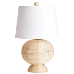 The NAPA HOME AND GARDEN Maye Rattan Hourglass Lamp with Shade features a wicker-style base and white shade, casting a warm glow on any wooden surface.