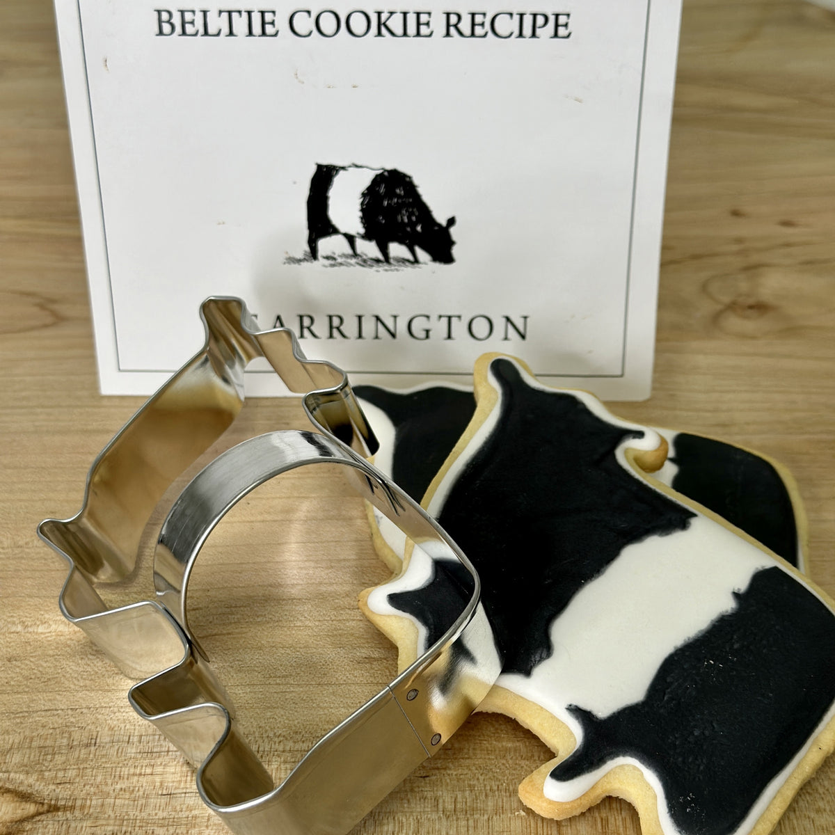 A cookie cutter from the FEARRINGTON SIGNATURE COLLECTION - BELTIE COOKIE CUTTER by AD RESOURCES is shaped like a cowboy boot, wrapped in clear plastic and tied with a black and white striped ribbon. Attached is a tag with the word &quot;FEARINGTON,&quot; an image of the cookie cutter, and a recipe card for Beltie Cow cookies.