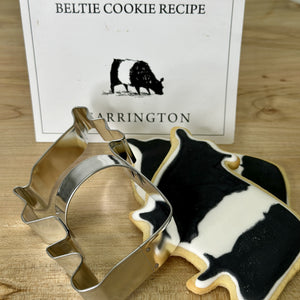 A cookie cutter from the FEARRINGTON SIGNATURE COLLECTION - BELTIE COOKIE CUTTER by AD RESOURCES is shaped like a cowboy boot, wrapped in clear plastic and tied with a black and white striped ribbon. Attached is a tag with the word "FEARINGTON," an image of the cookie cutter, and a recipe card for Beltie Cow cookies.