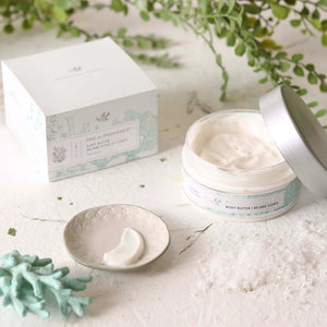 A clear jar with a silver lid contains BODY BUTTER - SEA SALT from EUROPEAN SOAPS, LLC, infused with Shea Butter. The label describes a sea salt scent and details 6.7 fl oz / 200 ml. The design features light green botanical illustrations on a white background, promising luxurious moisturization for your skin.