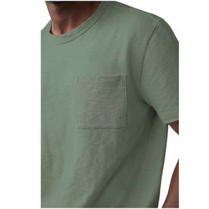A person wears the MACK WELDON Heavyweight Slub Cotton Pocket T-Shirt in Cactus, a light olive green relaxed fit short-sleeve tee with a chest pocket, shown cropped to the upper torso against a plain white background.