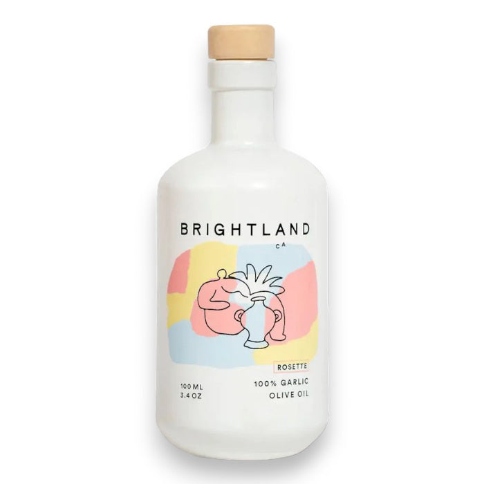 A white bottle with a wooden cap labeled "BRIGHTLAND - 'ROSETTE' GARLIC INFUSED OLIVE OIL," featuring an abstract colorful design with a pink figure holding a white vase. The text includes "ROSETTE," "100 ML," "3.4 OZ," and states that it contains 100% Garlic Olive Oil from early-harvest Frantoio olives grown on California’s Central Coast.