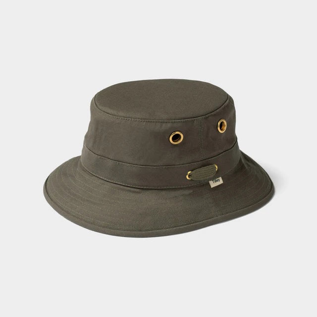 A person wearing the TILLEY - ICONIC T1 BUCKET HAT IN OLIVE with yellow eyelets and a white crew-neck shirt looks slightly to the side against a plain light background. The TILLEY hat offers UPF 50+ sun protection.