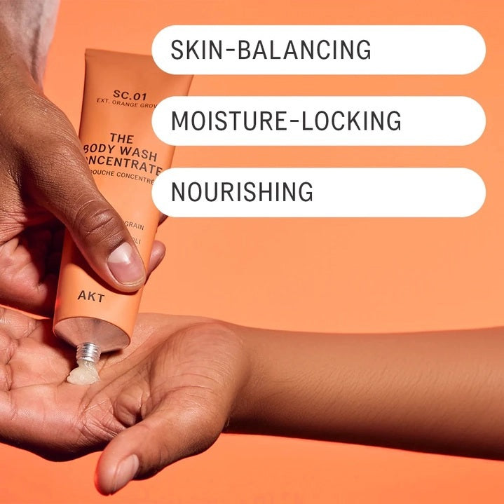 An orange tube of AKT LONDON - BODY WASH CONCENTRATE ORANGE GROVE and its matching box are displayed on beige tiles. The concentrated body wash features packaging that highlights ingredients such as mandarin, neroli, and vitamin E.