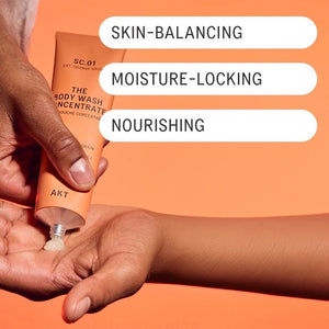 An orange tube of AKT LONDON - BODY WASH CONCENTRATE ORANGE GROVE and its matching box are displayed on beige tiles. The concentrated body wash features packaging that highlights ingredients such as mandarin, neroli, and vitamin E.