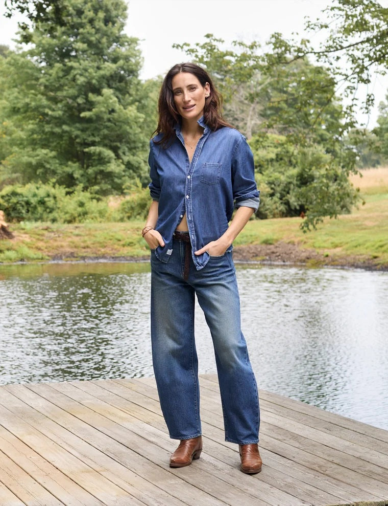 A close-up of a person wearing the FRANK & EILEEN Brennan Everyday Barrel Jean in California Vintage Denim 1993 Wash, paired with a loose blue shirt and one arm resting by their side.