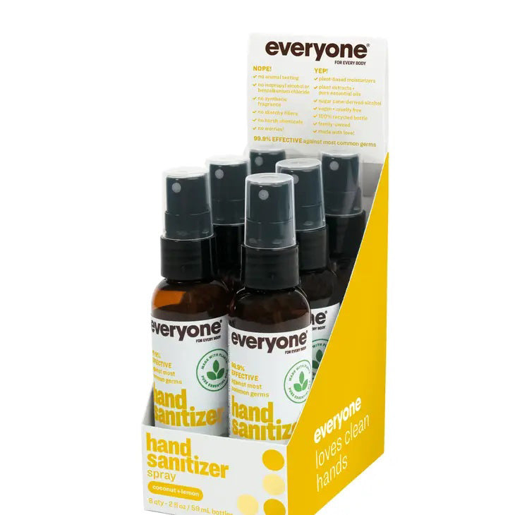 A brown leather bag is open, showing a bottle of Everyone For Everybody Coconut &amp; Lemon Hand Sanitizer Spray with 62% alcohol and a wallet inside. Adjacent to the bag are black sunglasses. The scene suggests preparedness for hygiene and travel or outdoor activities.