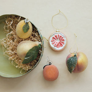 A green tin filled with paper shreds, a citrus slice ornament, a small round ornament, and a PEACH ORNAMENT WITH GLITTER.