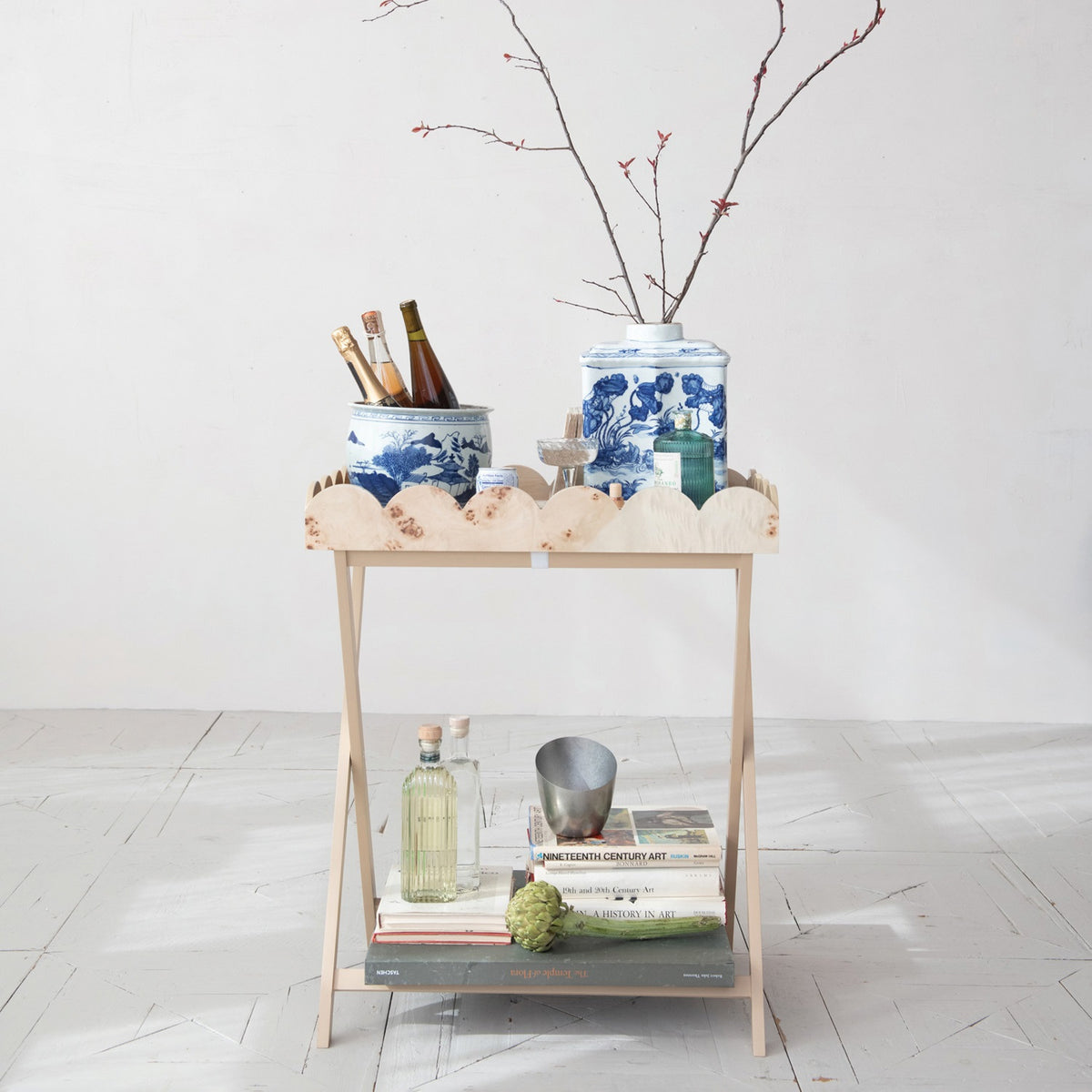 The CREATIVE COOP BURL WOOD VENEER FOLDING TABLE features crossed legs and a removable scalloped tray with a wavy rim and natural wood grain, blending charm with practical design.