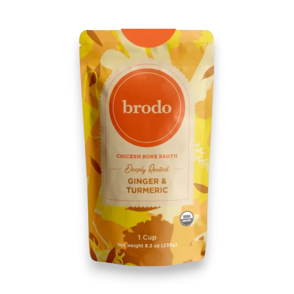 A carton of BRODO BROTH- DEEPLY ROOTED TURMERIC & GINGER BONE BROTH ORGANIC by BRODO BROTH COMPANY rests on a blue tray, surrounded by fresh turmeric and ginger roots—an ideal choice for those seeking a keto-friendly option.