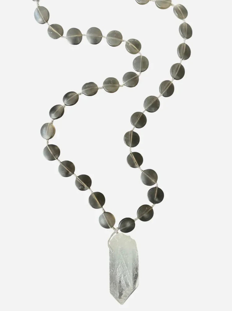 The ANN LIGHTFOOT Quartz and Smokey Glass Disc Pendant Necklace showcases round, dark smokey glass beads paired with a striking clear quartz pendant. Elegantly displayed on a white background, this 30-inch necklace by ANN LIGHTFOOT blends refined sophistication with natural allure.