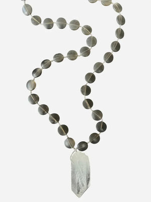 The ANN LIGHTFOOT Quartz and Smokey Glass Disc Pendant Necklace showcases round, dark smokey glass beads paired with a striking clear quartz pendant. Elegantly displayed on a white background, this 30-inch necklace by ANN LIGHTFOOT blends refined sophistication with natural allure.
