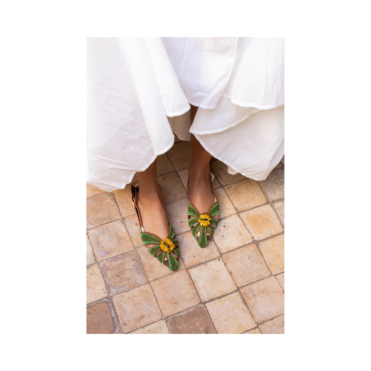 The MEHER KAKALIA - QUEEN DORIS SLING BACK in HAWAIIAN SANDS NILE showcases vibrant green and orange woven patterns with a traditional embroidery style, decorative toe knot, adjustable ankle strap, closed heel, and branded insole.