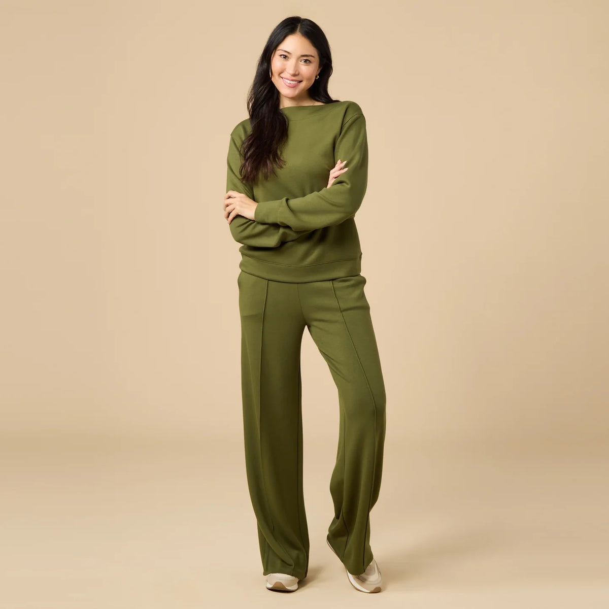 A woman wears a SOFTIES - DREAMTECH BOAT NECK WITH PINTUCK PANT SET in olive green, featuring a long-sleeve boat neck top and matching wide-leg pintuck pants.
