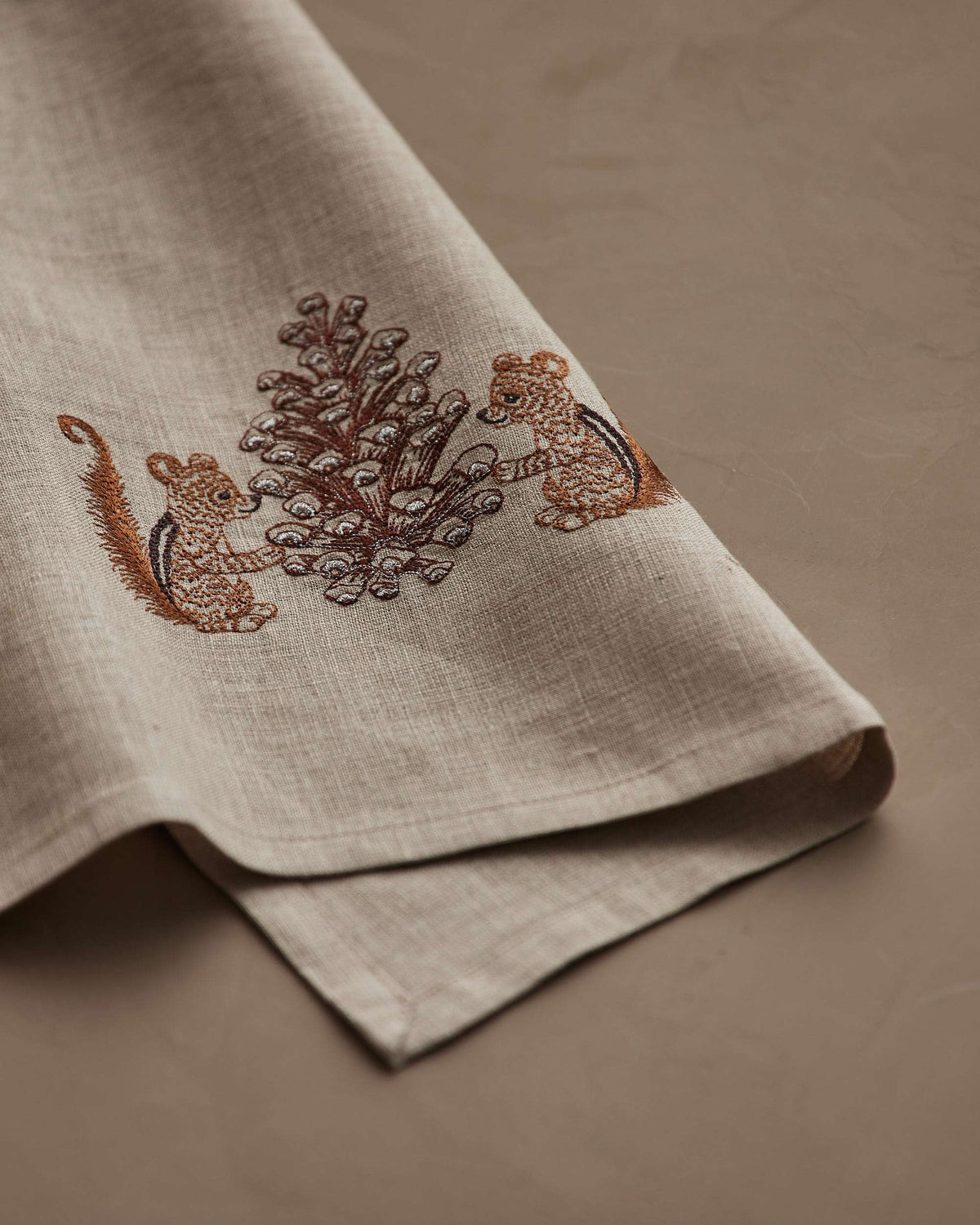 CHIPMUNKS WITH PINECONE LINEN TEA TOWEL by CORAL & TUSK featuring embroidered chipmunks holding a large, stitched pinecone.