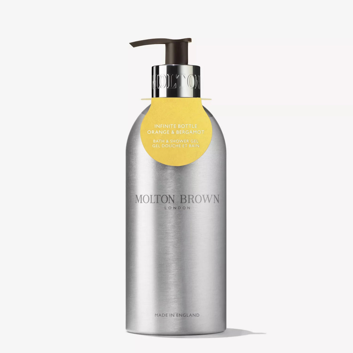 A silver recycled aluminium MOLTON BROWN bottle with pump, labeled "ORANGE &amp; BERGAMOT BODY WASH INFINITE BOTTLE," features citrus and orange neroli fragrance and a yellow tag hanging from the neck.