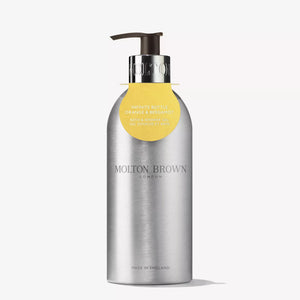 A silver recycled aluminium MOLTON BROWN bottle with pump, labeled "ORANGE & BERGAMOT BODY WASH INFINITE BOTTLE," features citrus and orange neroli fragrance and a yellow tag hanging from the neck.