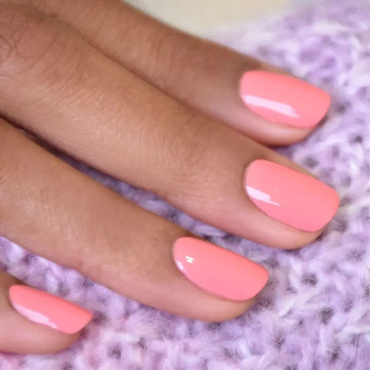 A hand with short, neatly manicured nails painted with MANUCURIST - GREEN™ Nail Polish in Pink Paradise by MANUCURIST INC rests on a cream-colored knitted fabric.