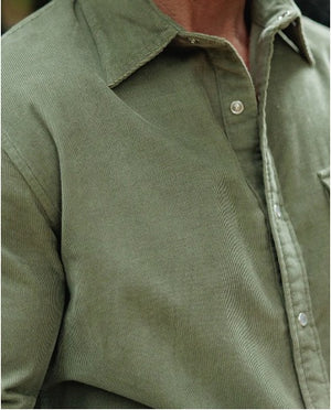 A smiling man with a gray beard, wearing the CRIQUET Long Sleeve Corduroy Pearl Snap Shirt in Olive and a brown cowboy hat, stands by the open door of a red and white vehicle.