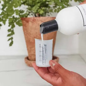 The LAUNDRESS - MEASURING CUP by THE LAUNDRESS is a white plastic measuring cup featuring ounce and milliliter markings on the side, making it ideal for accurately measuring THE LAUNDRESS detergents and other fabric care products.