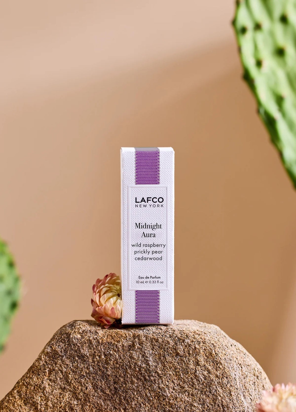 A person holds a 10ml bottle of LAFCO Fine Fragrance, Midnight Aura, on their bare shoulder against a soft purple background.