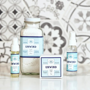 The 2 fl oz BAUDELAIRE - UNWIND SHOWER MIST comes in a clear spray bottle with a blue label and offers a citrus aroma. It's alcohol-free and enriched with essential oils for aromatherapy bliss, making it perfect for essential oil shower mists.