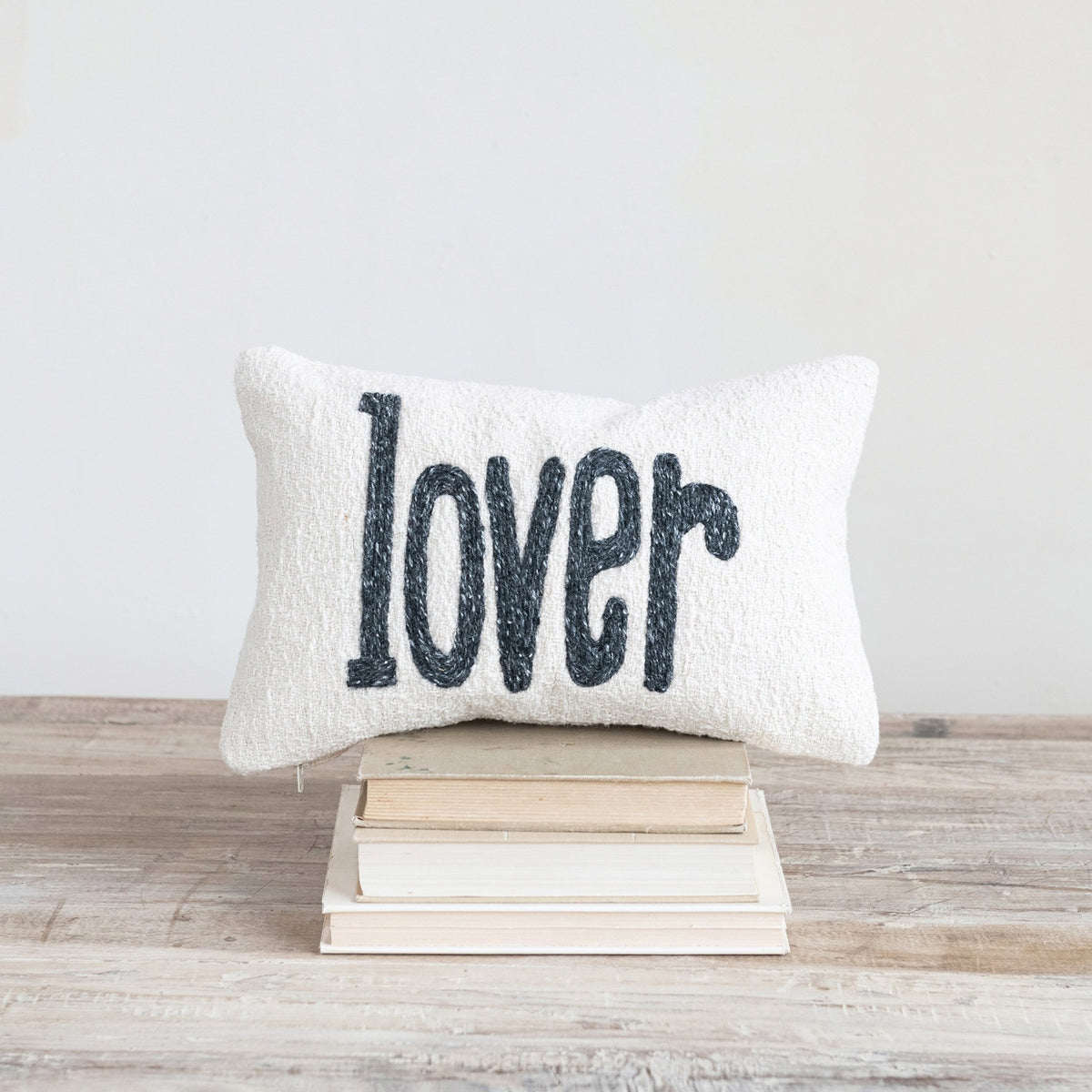 The “LOVER” LUMBAR PILLOW by CREATIVE COOP is a cream-colored cotton slub accent pillow with “lover” in bold black lowercase letters, perfect as a charming decorative piece.