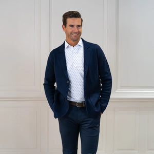 The COLLARS AND CO FEATHERWEIGHT FLEX POLO IN ORACLE WHITE features white fabric with a repeating pattern of small blue 3x3 dot squares. Slightly creased at the center, its 6-way stretch design ensures all-day comfort.