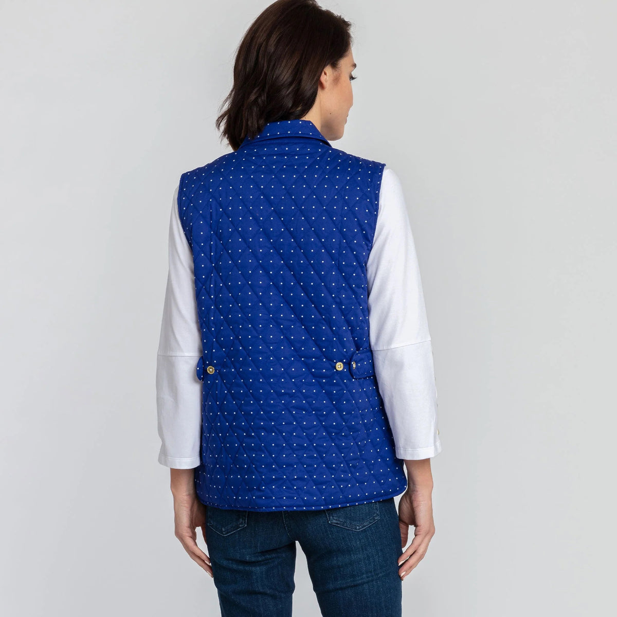 A woman with short brown hair is wearing the HINSON WU - LAUREN REVERSIBLE VEST in bright blue, paired with a white, long-sleeve blouse that features buttons on the cuffs. She completes her outfit with blue jeans and stands against a plain white background.