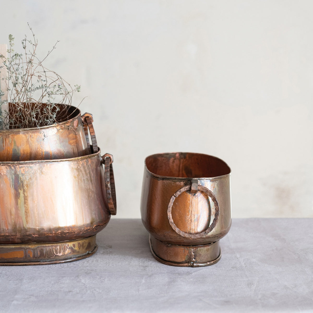 The OVAL METAL PLANTER WITH RING HANDLES, SMALL by CREATIVE COOP features a vintage oval design with ring handles and a charming, aged copper finish—an ideal accent for farmhouse decor.