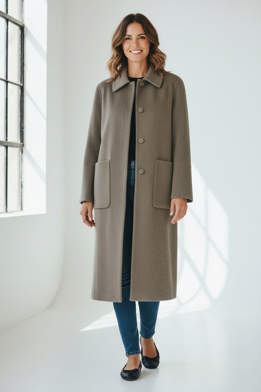 A woman poses confidently with one hand in her pocket, wearing the SEVENTY VENEZIA - WOOL BLEND LONG COAT by SEVENTY over a striped shirt, brown trousers, and brown shoes against a plain background.