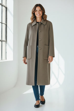 A woman poses confidently with one hand in her pocket, wearing the SEVENTY VENEZIA - WOOL BLEND LONG COAT by SEVENTY over a striped shirt, brown trousers, and brown shoes against a plain background.