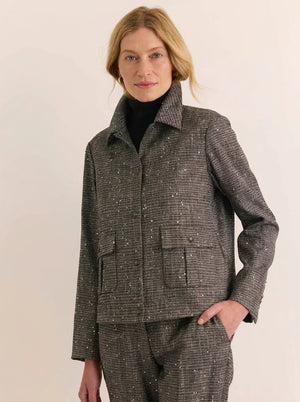 A woman wears a charcoal gray HINSON WU - HANNAH LONG SLEEVE TWEED JACKET WITH SEQUINS, a black turtleneck, and matching tweed trousers, holding a black clutch.