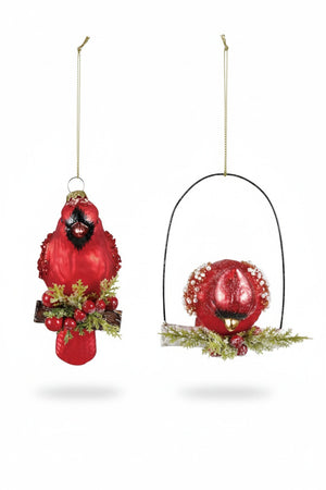 Two Creative Co-op HAND PAINTED CARDINAL ORNAMENT WITH BEADS AND GLITTER pieces hang from a branch, one on a perch and one suspended vertically, both decorated with beads and berries.
