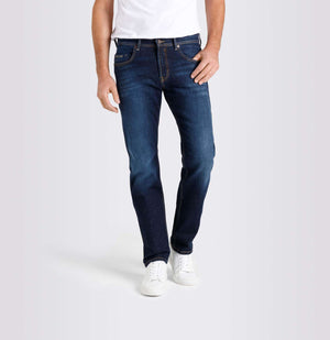 A person wearing MAC JEANS - BEN AUTHENTIC DENIM REGULAR FIT DARK VINTAGE WASH by MAC, paired with a white t-shirt and white sneakers, stands against a plain light gray background.