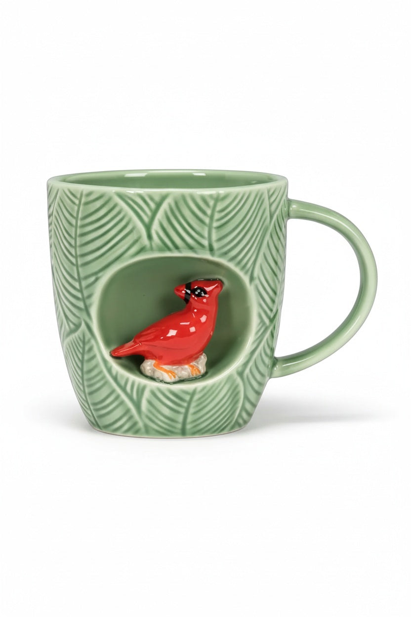 Green stoneware CARDINAL MUG WITH ALCOVE featuring a leaf pattern and a small, recessed alcove containing a red cardinal figure.