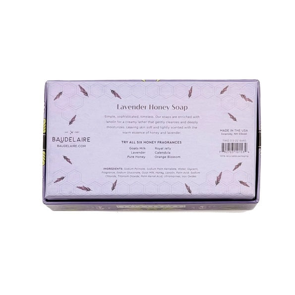 The BAUDELAIRE - LAVENDER HONEY SOAP 3.5 OZ, 2 BAR GIFT BOX features two hexagonal, triple-milled soaps with a beehive design, nestled in a decorative purple floral box and partially opened to reveal the lavender-colored bars inside.